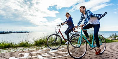 A young couple biking along the ocean with the benefit of having permanent life insurance.