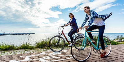 A young couple biking along the ocean with the benefit of having permanent life insurance. 