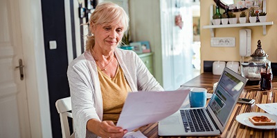 Senior lady in yellow shirt looks at financials in her kitchen