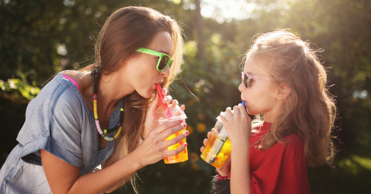 Mother and young daughter wearing sunglasses and drinking tea outside