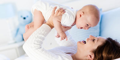 A mom and her baby laughing together as she holds him in the air.