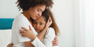 Mom hugging young daughter, looking very sad.