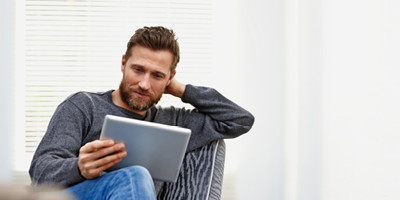 Man with a beard and a gray shirt studying something on a tablet.