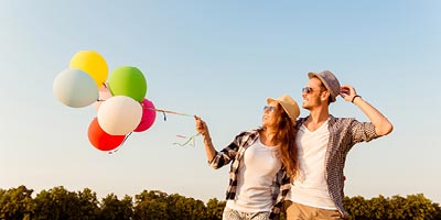 Young couple walking together holding colorful balloons that are flying in the wind.
