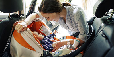 Young mother fastening her baby’s carseat into the car and smiling at her baby.