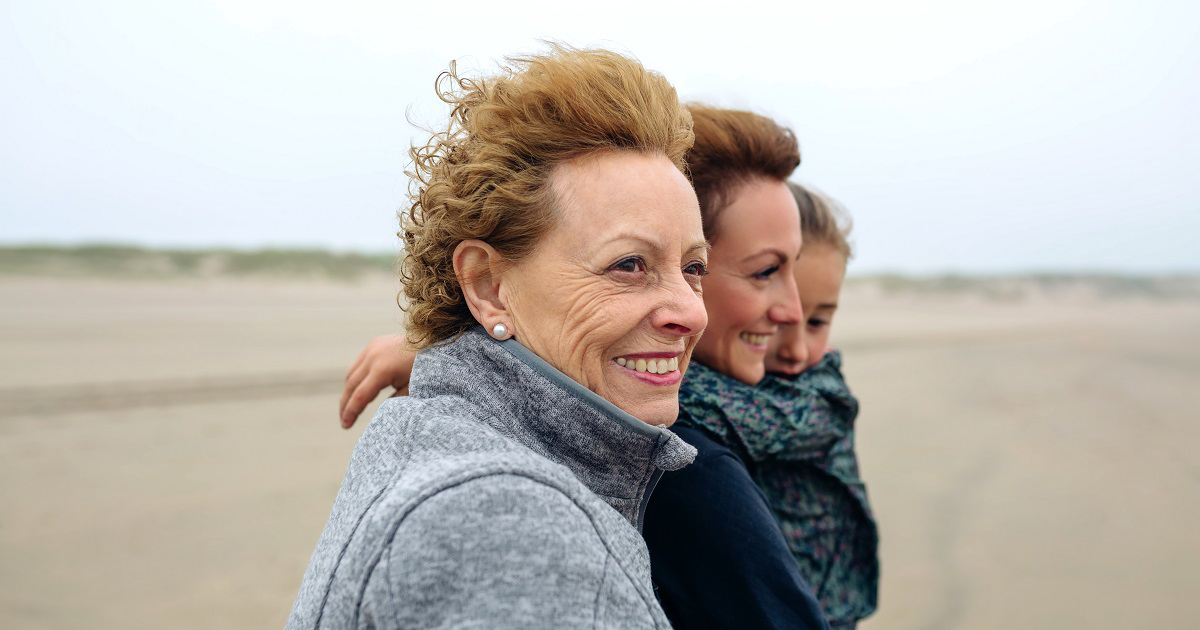 Grandmother standing with daughter and grandaughter on a windy beach.