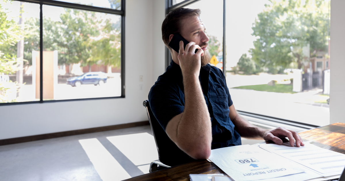 Man on smartphone at desk with credit report in front of him
