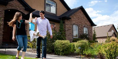 Happy mom and dad swing daughter between them in front of big, new house