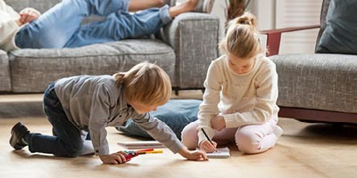 Brother and sister sitting on living room floor writing and playing