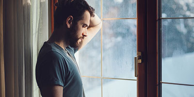  Man in his thirties looking sad, staring out a window.