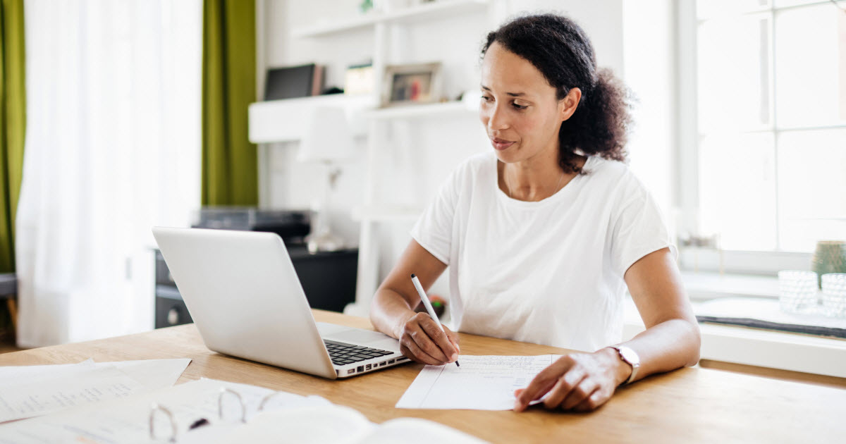 Woman sitting at desk with laptop and binder of papers