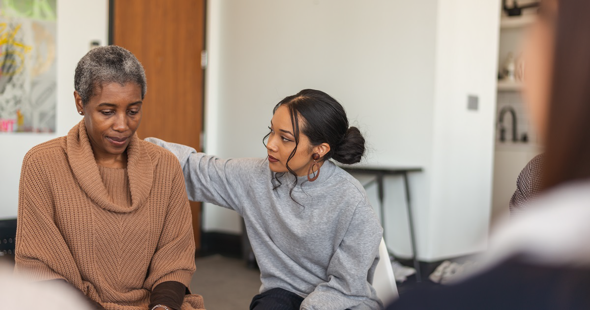 Young African American female comforts grieving woman at support group.