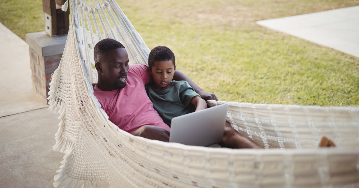 Father and son in hammock looking at laptop