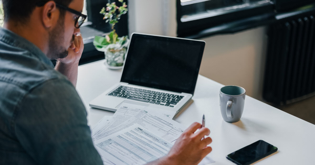 Man sitting at desk looking at tax forms and laptop