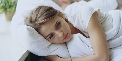 Woman looking very depressed lying in bed and staring into space.
