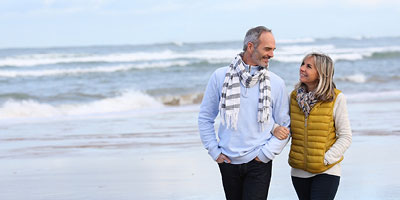 Husband and wife smile at each other while they walk together along the beach