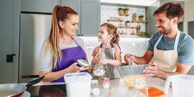 Mom and dad with their young daughter in the kitchen preparing a meal