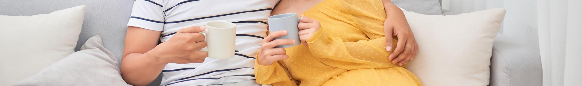 Husband and wife sitting on couch drinking coffee and talking about managing their money in their marriage. 