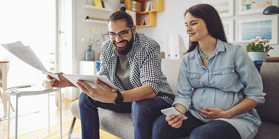 Happy man and pregnant woman sitting on a couch looking at paperwork and a tablet