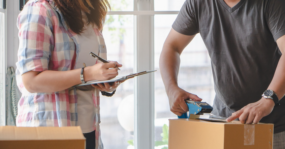 Man taping a box standing with woman using a moving checklist.