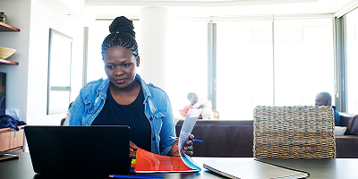 Woman sitting at counter with laptop while family relaxes on couch in background