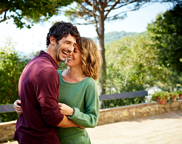 Husband and wife laughing and embracing outdoors.