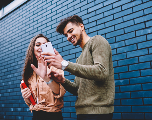 Male and female college students laughing and looking at smartphone.