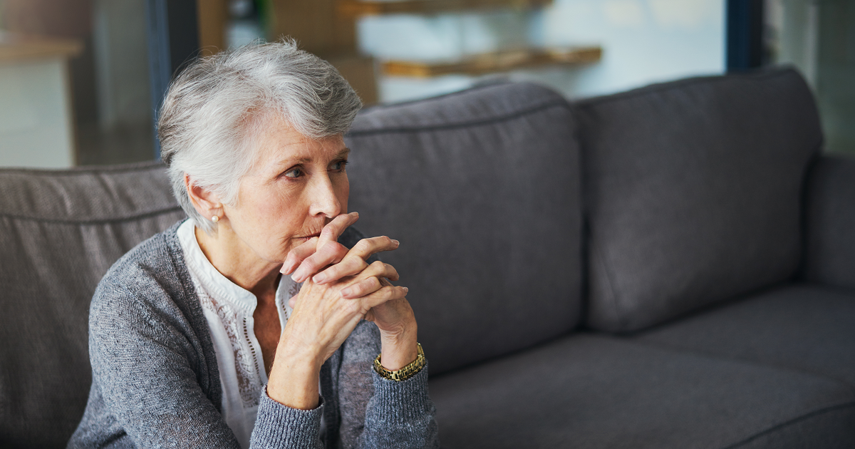 Worried senior woman sitting on couch.