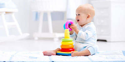 Baby sitting up, playing with a stacking toy.