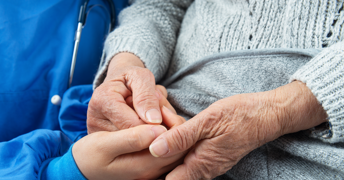 Close up of a hospice worker holding an elderly patient’s hands.