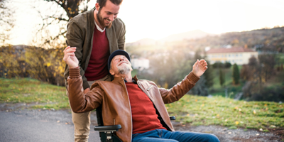 Adult son taking father for an outdoor stroll in his wheelchair.