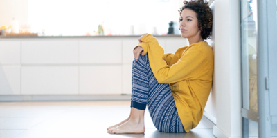 Young woman wearing pajamas sits on the kitchen floor. 