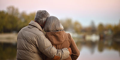 An older couple embraces while gazing off into the distance