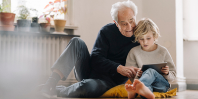 Grandfather sitting with his grandson on the floor, looking at a tablet together.