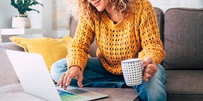 Woman uses her laptop on the couch while drinking coffee