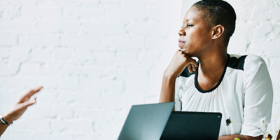 Middle-aged African-American woman sitting in front of her laptop and intensely thinking.