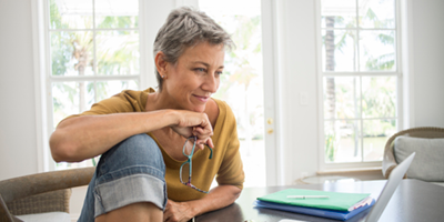 Women holding a pair of glasses in her hand gazes thoughtfully at computer screen.
