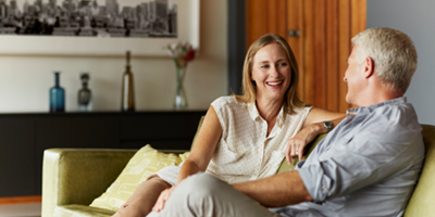 Middle-aged female and male seated on a couch facing each other and having a conversation.