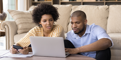 African American couple sitting on their living room floor evaluating long-term care insurance on a laptop.