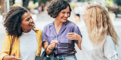 Three woman who are good friends walking in the street, laughing and talking together.
