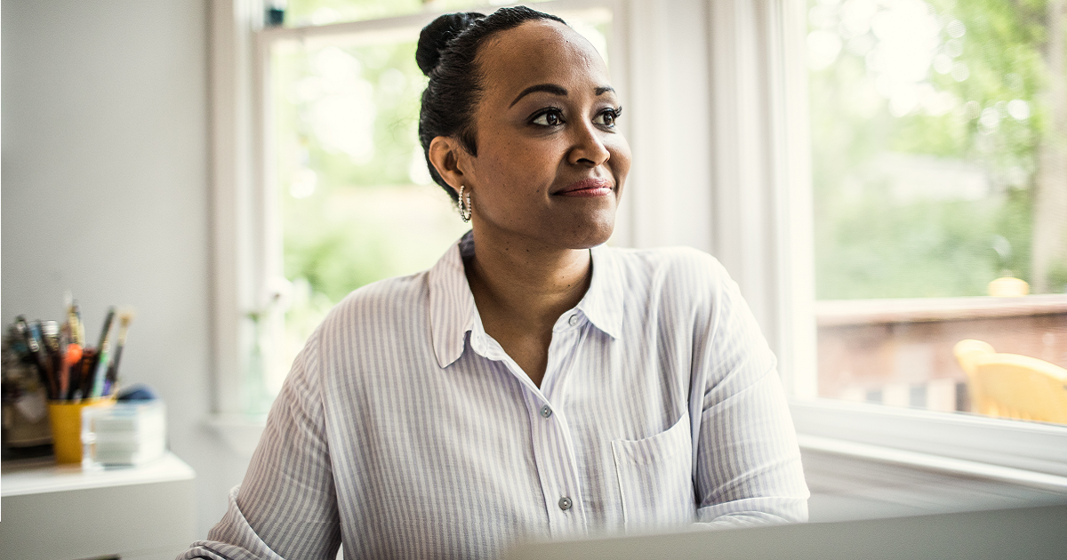 Middle-aged Black woman sitting in front of laptop and looking out window