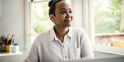 Middle-aged Black woman sitting in front of laptop and looking out window