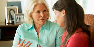 Senior woman in a green short speaking with her daughter on the couch, looking serious.