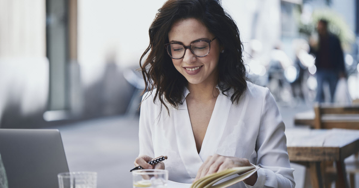 Woman sitting at an outdoor table with laptop and notebook