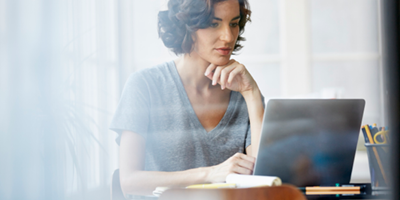 Woman in a gray t-shirt looking up something on her laptop.