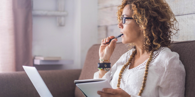 Woman with curly hair and a white shirt, chewing on a pencil and thinking about retirement.