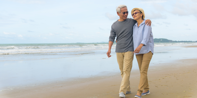 A senior adult couple walking along the beach and laughing because they have planned well for their retirement.