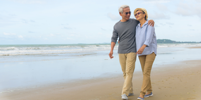 A senior adult couple walking along the beach and laughing because they have planned well for their retirement. 