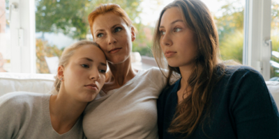 A woman and two daughters huddled on a couch together staring into the distance.