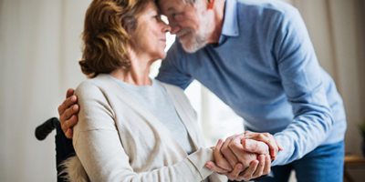 Senior husband touching foreheads with wife in wheelchair